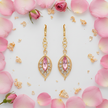 Flat lay of gold plated filigree leaf drop earrings with pink crystal on white surface with rose petals