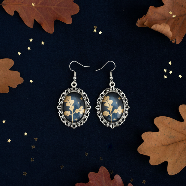 Gold oak leaf cabochon drop earrings on dark navy velvet with autumn leaves and gold star confetti
