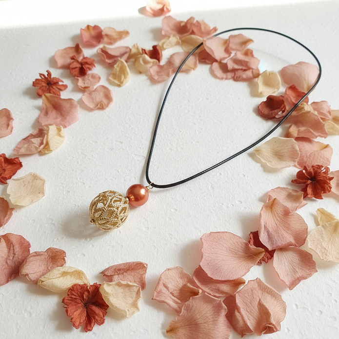Copper pearl and gold filigree cage pendant necklace flat lay with flower petals