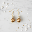 Gold pearl drop earrings flat lay on white marble