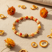 Orange marbled bead and gold heart bracelet flat lay on sandy linen with dried orange flowers