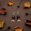 Burgundy crystal teardrop and leaf charm earrings flat lay on autumn linen with dried leaves