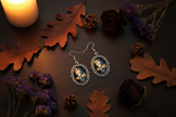 Gold oak leaf cabochon earrings on dark wood with autumn oak leaves and pine cones