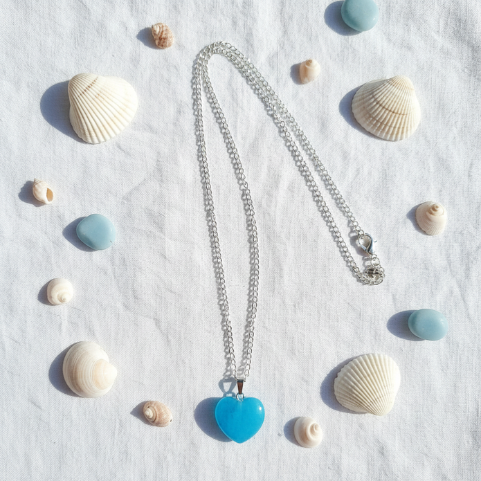 Turquoise blue glass heart pendant necklace coastal flat lay with shells and pebbles
