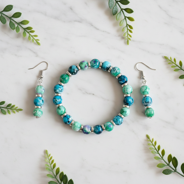 Flat lay of turquoise and green marbled bracelet and earrings set with green leaf props