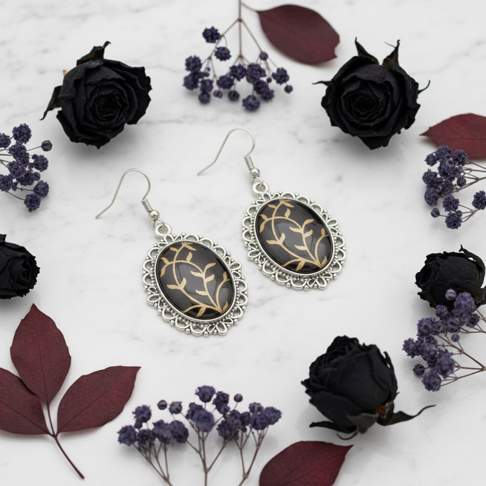 Large black and gold oval drop earrings styled on marble with dark dried flowers