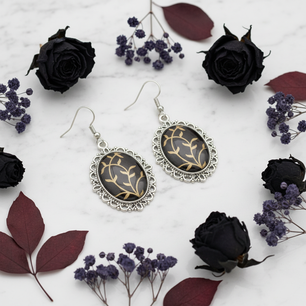 Large black and gold oval drop earrings styled on marble with dark dried flowers