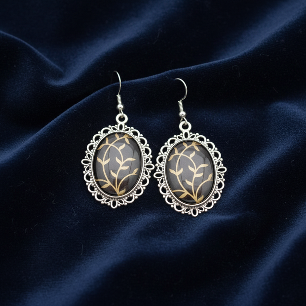 Black and gold oval drop earrings flat lay on dark velvet