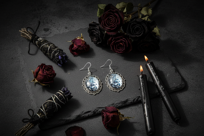 Iridescent rose spiderweb cabochon earrings on dark stone with black roses and gothic candles