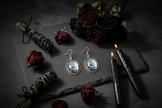 Iridescent rose spiderweb cabochon earrings on dark stone with black roses and gothic candles