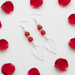 Flat lay of red glass bead and crystal leaf drop earrings with red rose petal props