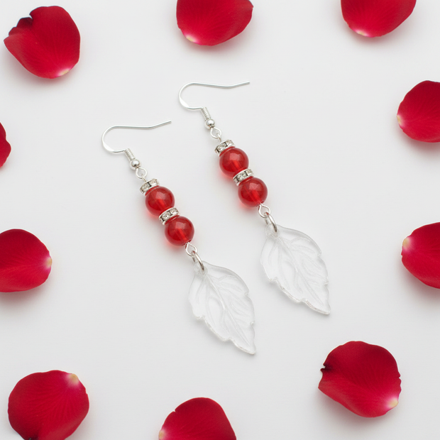 Flat lay of red glass bead and crystal leaf drop earrings with red rose petal props