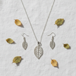 Silver filigree leaf necklace and earrings set flat lay on white linen with autumn leaves