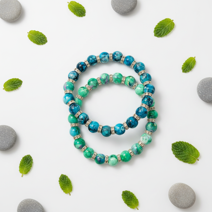 Flat lay of two turquoise and green marbled beaded bracelets with leaf and pebble props