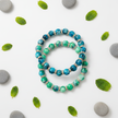 Flat lay of two turquoise and green marbled beaded bracelets with leaf and pebble props