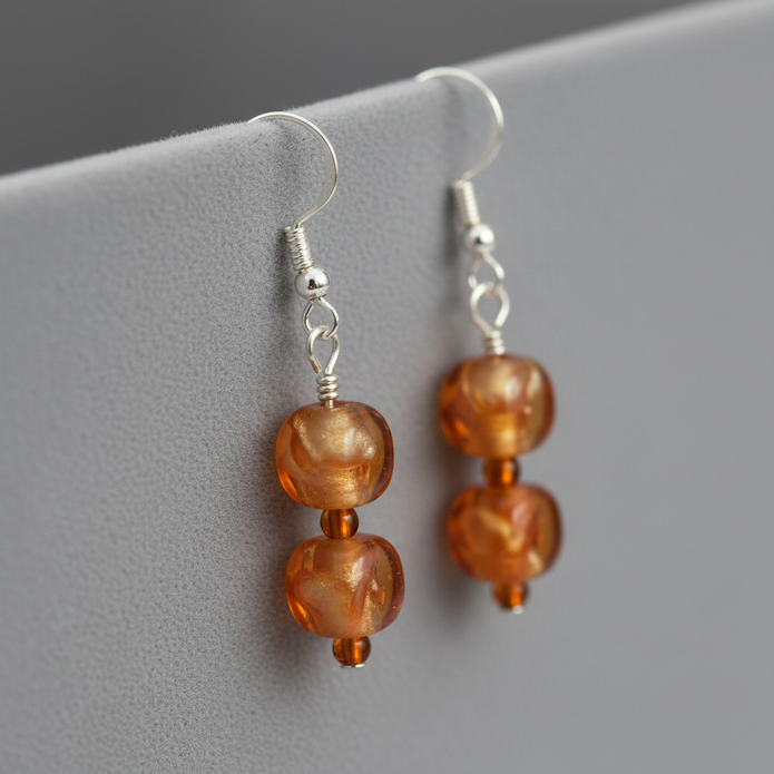 Close-up of amber orange and gold drop earrings on silver hooks