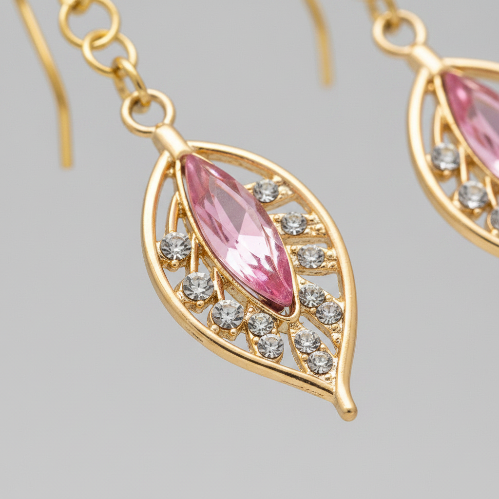 Close-up macro of gold plated filigree leaf drop earrings showing pink marquise crystal and diamante detail