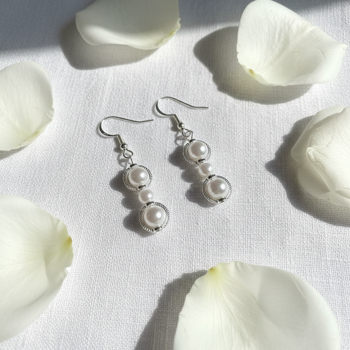Pearl bead filigree circle drop earrings flat lay on white linen with white rose petals