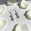 Pearl bead filigree circle drop earrings flat lay on white linen with white rose petals