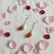 Red and cream oval bead drop earrings flat lay with pink and red flower petals on white linen