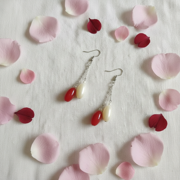Red and cream oval bead drop earrings flat lay with pink and red flower petals on white linen