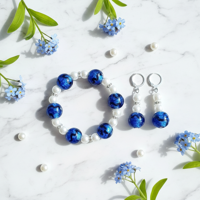 Flat lay of cobalt blue and pearl bracelet and earrings set on marble with pearl and flower props
