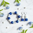 Flat lay of cobalt blue and pearl bracelet and earrings set on marble with pearl and flower props