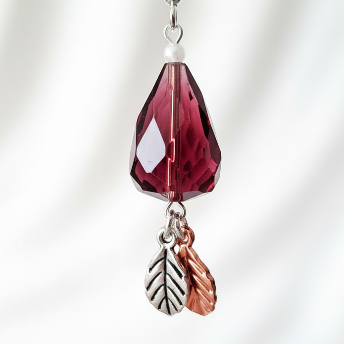 Close-up detail of burgundy faceted crystal teardrop with silver and rose gold leaf charms