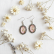 Pink floral cabochon drop earrings flat lay on white linen with dried flowers