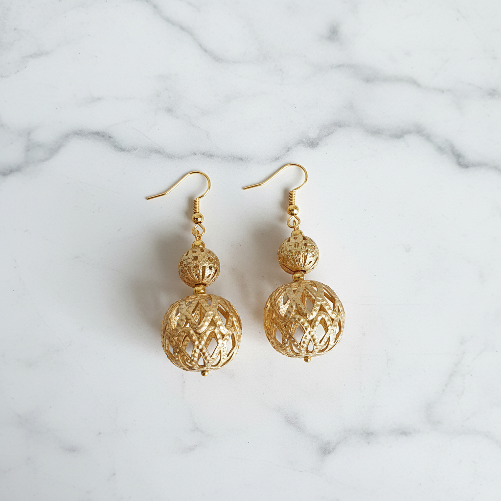 Gold filigree cage bead drop earrings flat lay on white marble
