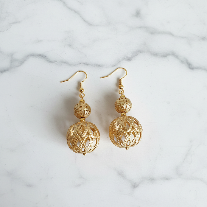 Gold filigree cage bead drop earrings flat lay on white marble