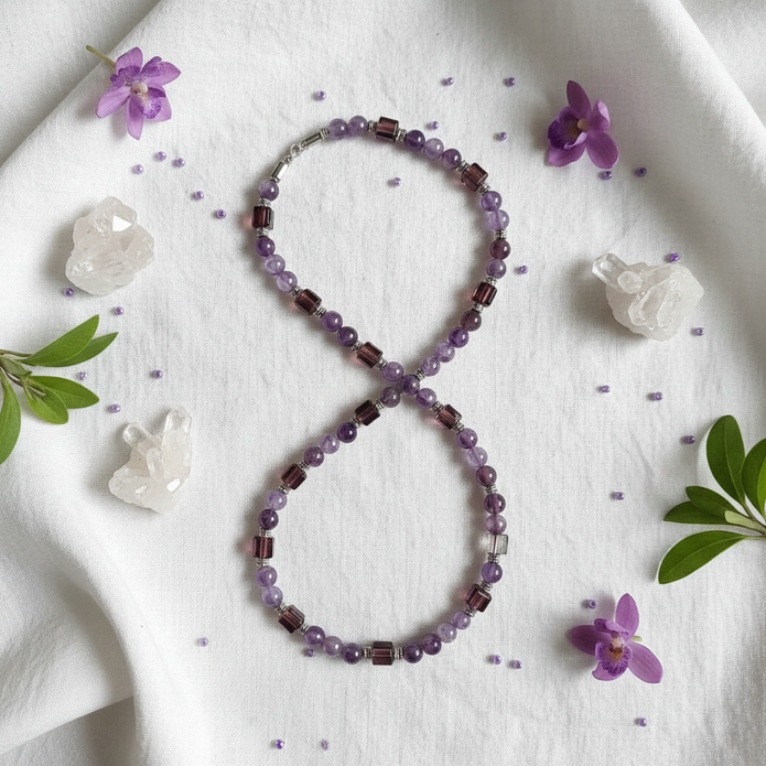 Flat lay of purple and brown beaded necklace with silver spacers on white linen with purple flowers