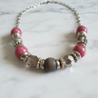 Close-up of rescued and remade pink crackle and ornate gold silver bead necklace on white marble