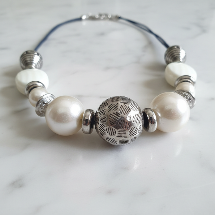 Close-up of rescued and remade pearl and antique silver engraved bead necklace on white marble