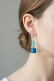 Model wearing blue glass cube and aqua bead drop earrings with silver daisy spacers
