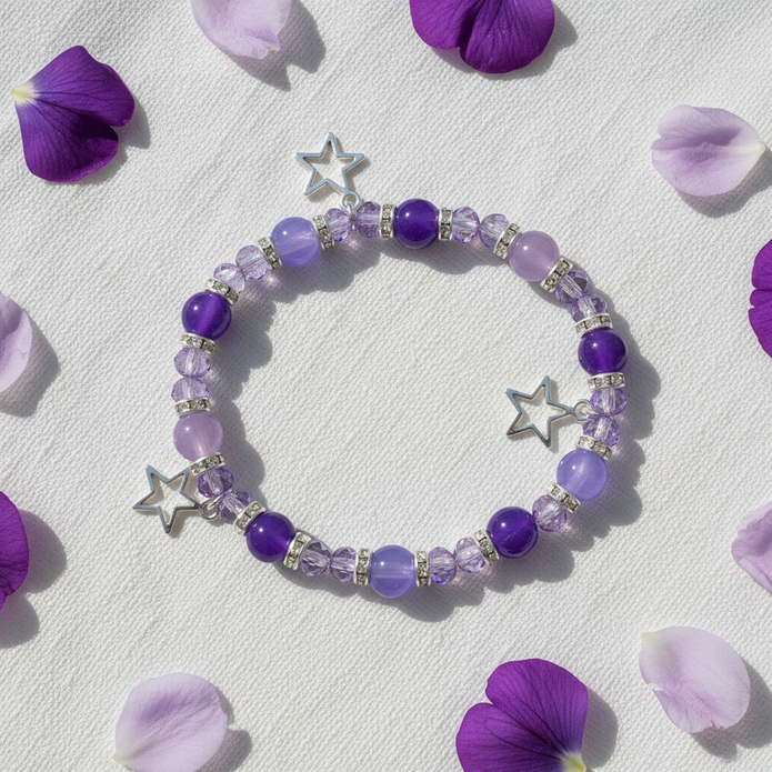Purple and lilac star charm bracelet flat lay on white linen with purple flower petals