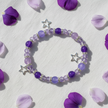 Purple and lilac star charm bracelet flat lay on white linen with purple flower petals