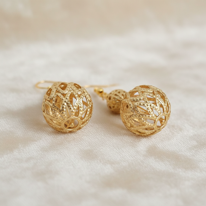 Gold filigree cage bead drop earrings styled on cream fabric