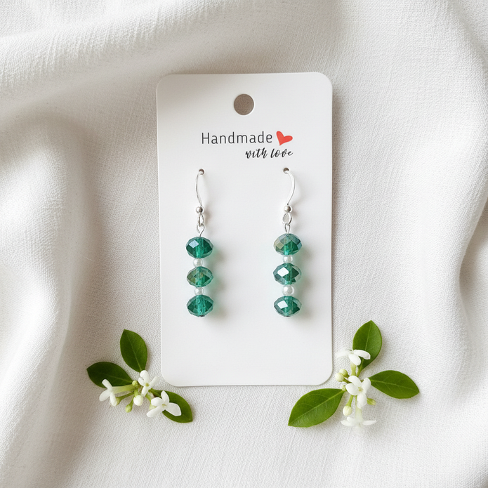 Green and white sterling silver crystal earrings flat lay on white linen with green leaves