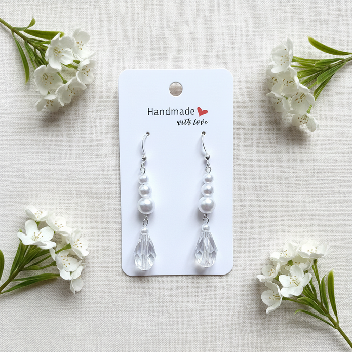 Sterling silver pearl and crystal teardrop earrings flat lay on white linen with flowers