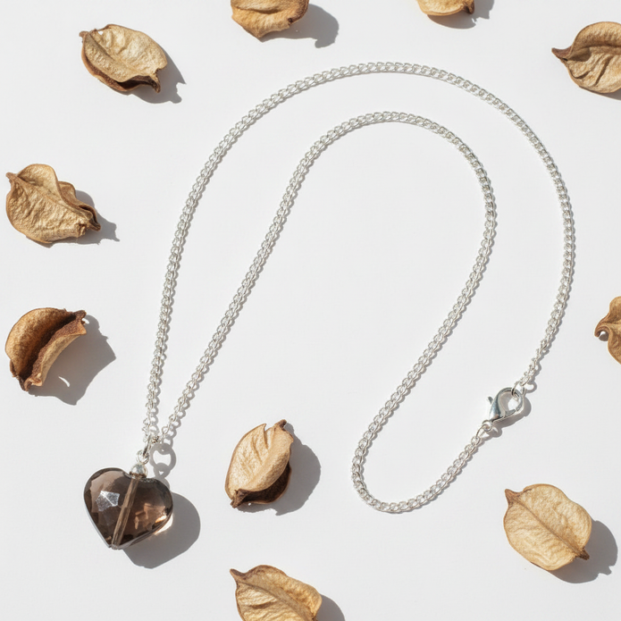 Smoky brown glass heart pendant necklace flat lay with dried petals on white background