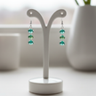 Green and white sterling silver earrings displayed on white ceramic jewellery stand