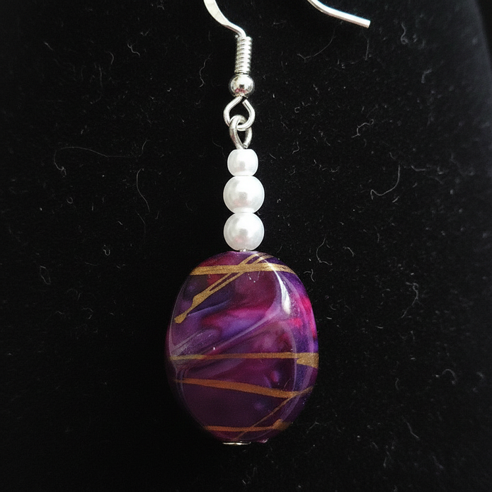 Close-up detail of rescued plum drop earring showing gold swirl bead and pearl accents