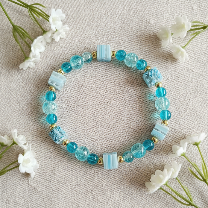 Teal crackle bead bracelet flat lay with white flowers on linen
