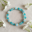 Teal crackle bead bracelet flat lay with white flowers on linen