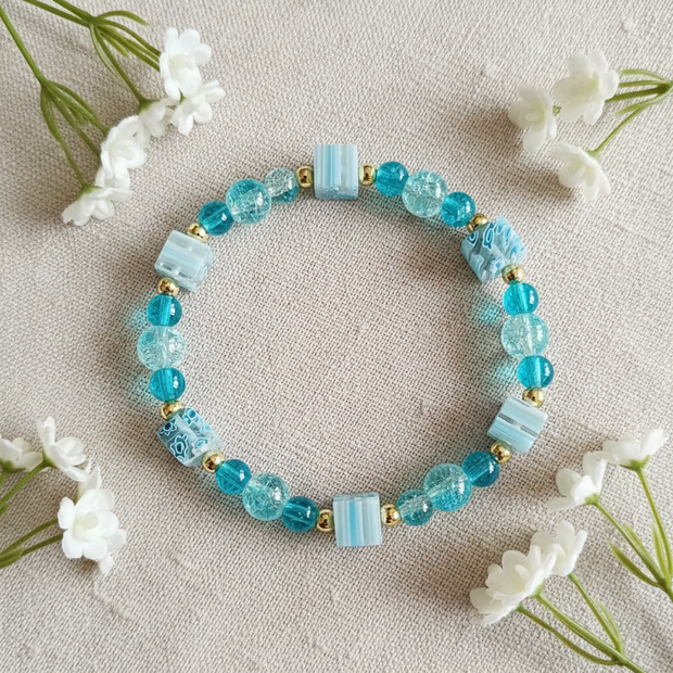 Teal crackle bead bracelet flat lay with white flowers on linen