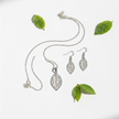 Silver filigree leaf necklace and earrings set flat lay with green leaves on white background