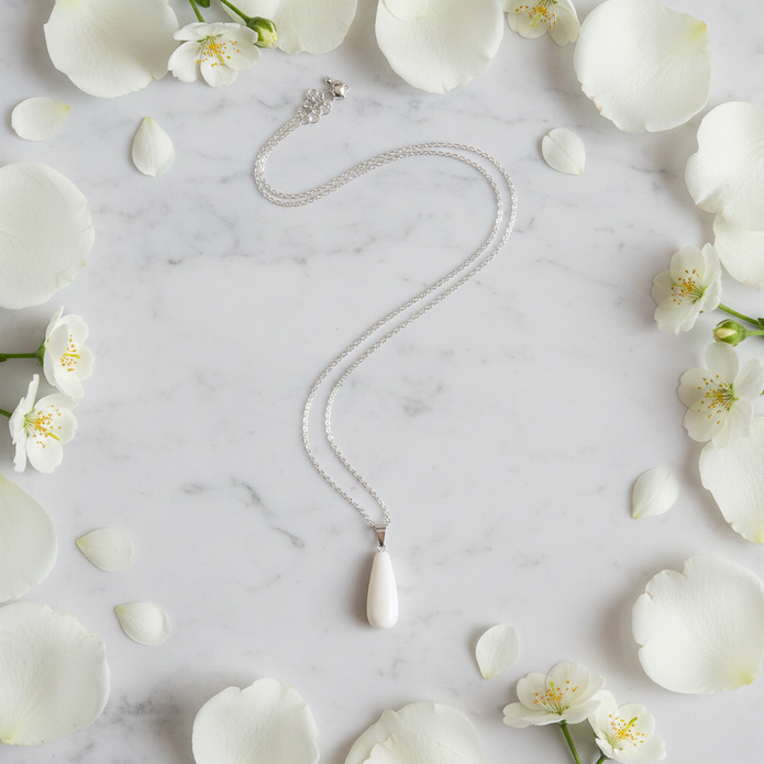 White teardrop necklace flat lay with cream flower petals