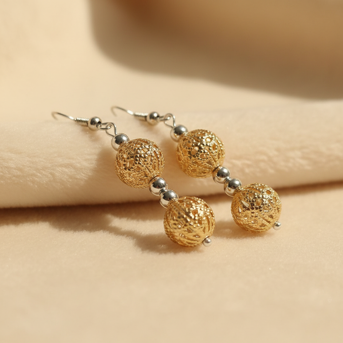 Gold filigree double cage bead drop earrings styled on cream fabric