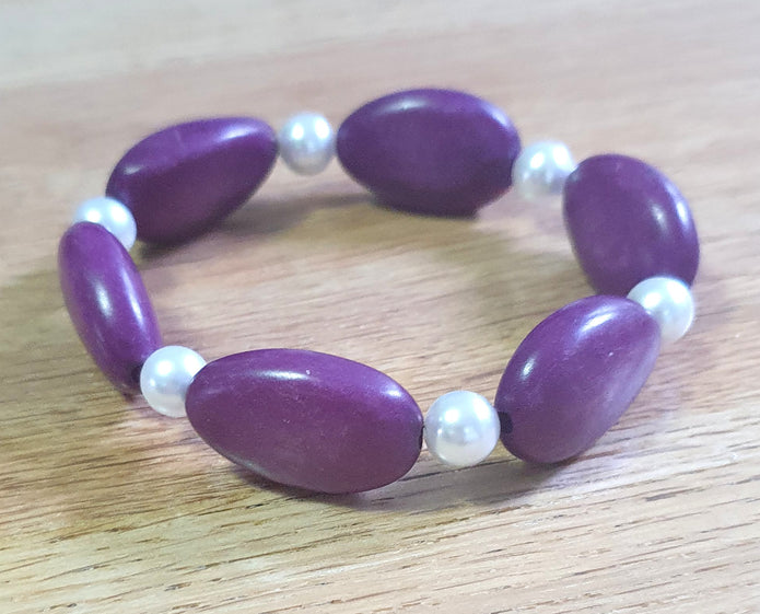 Purple beaded bracelet with white pearls on a wooden surface